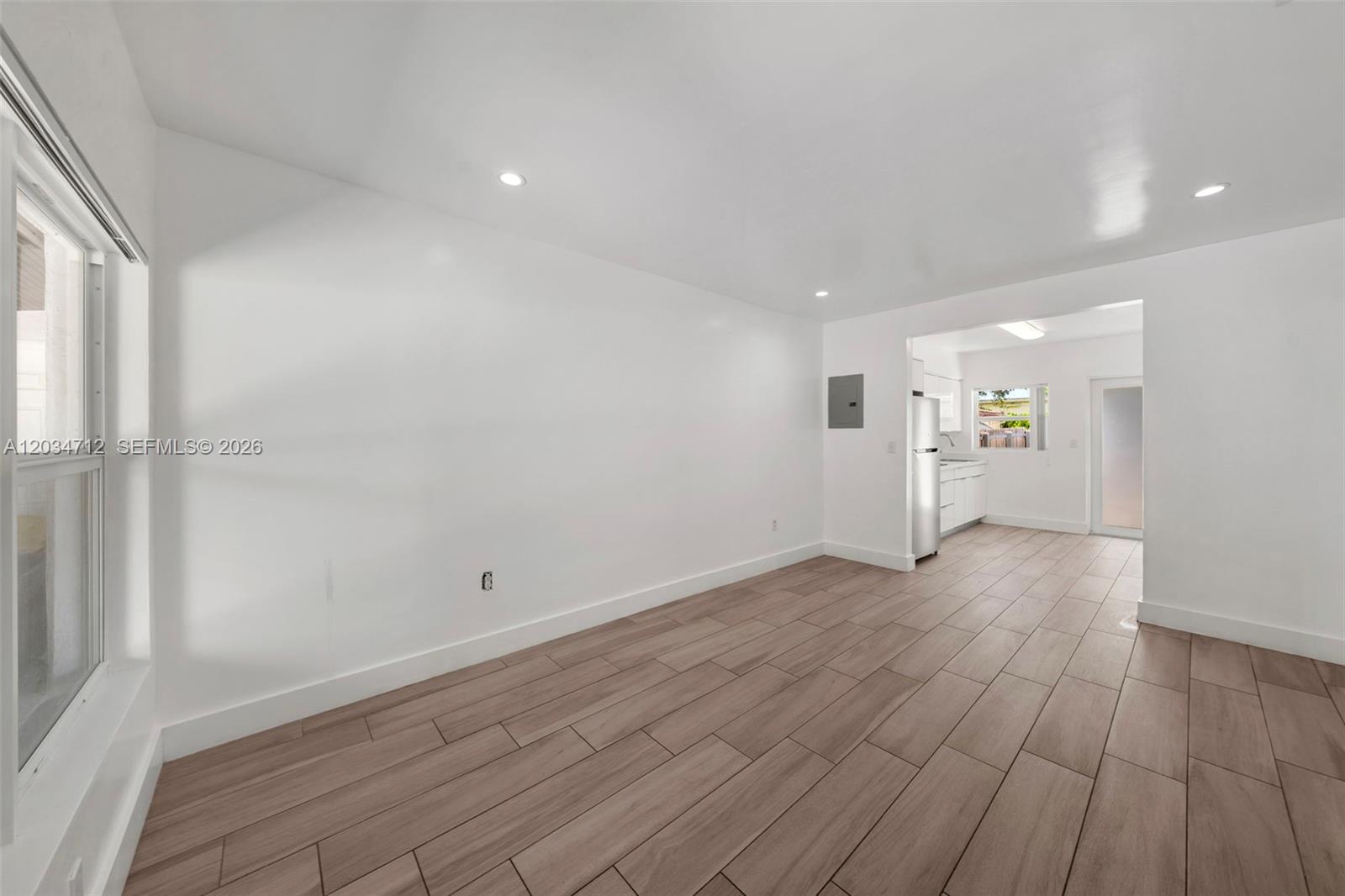 A bright, empty room with wood-look tile flooring leads into a small kitchen area — 520 NW 104th St # 522, Miami FL 33150, MIAMI, FL