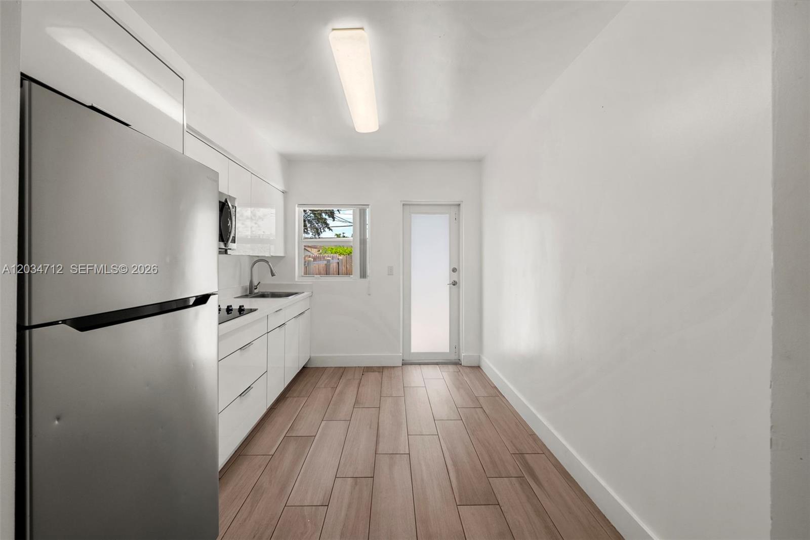 A minimalist kitchen features white cabinetry, stainless steel appliances, and light wood-look flooring — 520 NW 104th St # 522, Miami FL 33150, MIAMI, FL