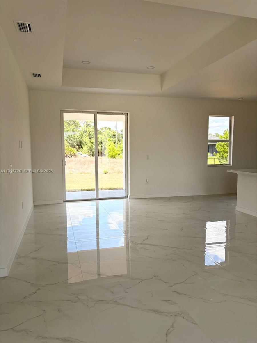An empty room features white marble-look tile flooring, a tray ceiling, and sliding glass doors — 4118 4th ST SW, Lehigh Acres FL 33976, LEHIGH ACRES, FL