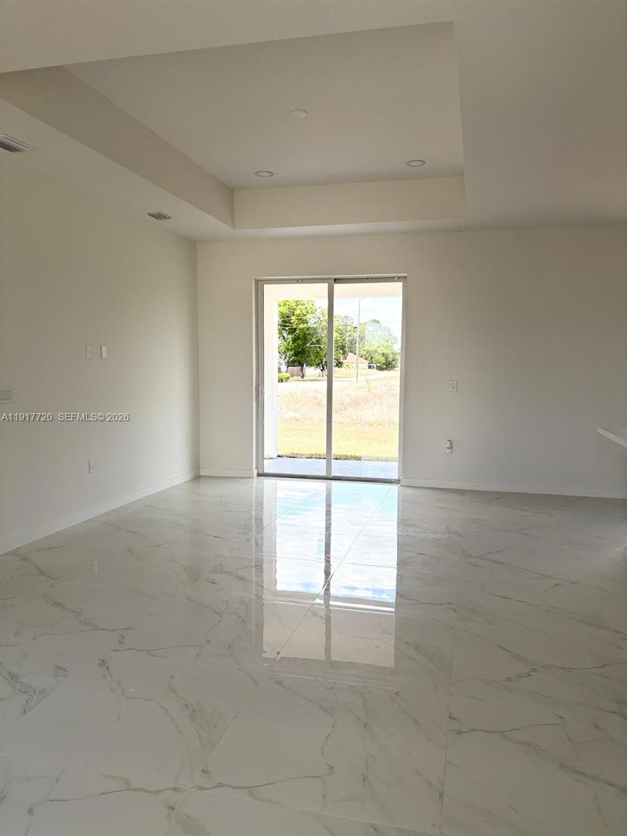 A bright room features white walls, a tray ceiling, and polished marble-look tile flooring — 4118 4th ST SW, Lehigh Acres FL 33976, LEHIGH ACRES, FL
