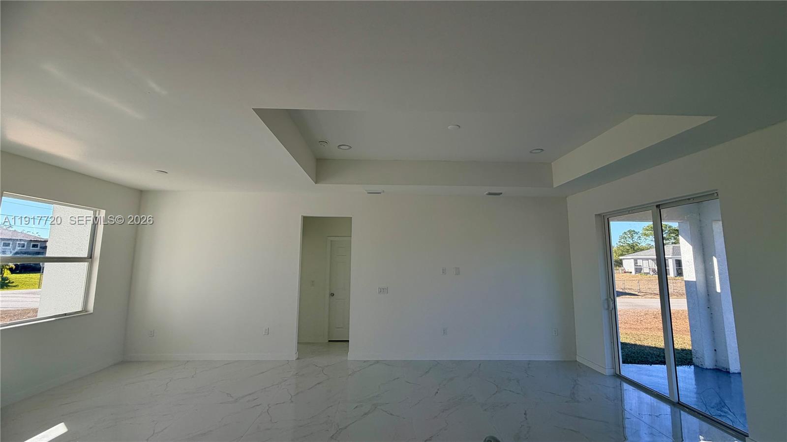 A bright, empty living room features white walls, marble-look tile flooring, and a tray ceiling — 4118 4th ST SW, Lehigh Acres FL 33976, LEHIGH ACRES, FL