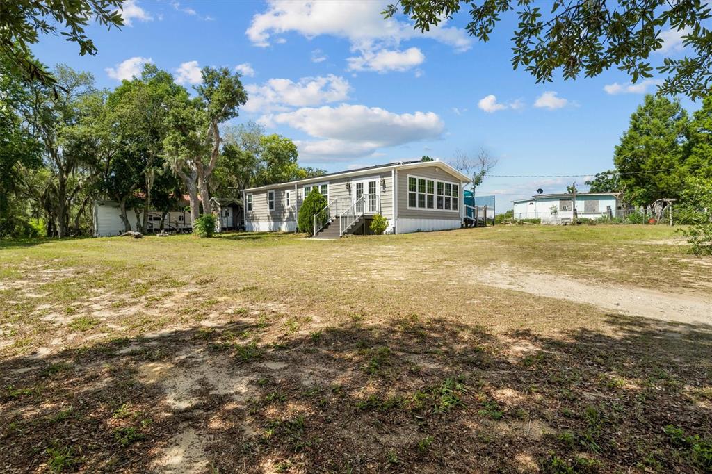 A single-story manufactured home sits on a large, grassy lot surrounded by trees — 2742 MASTERPIECE ROAD, LAKE WALES, FL