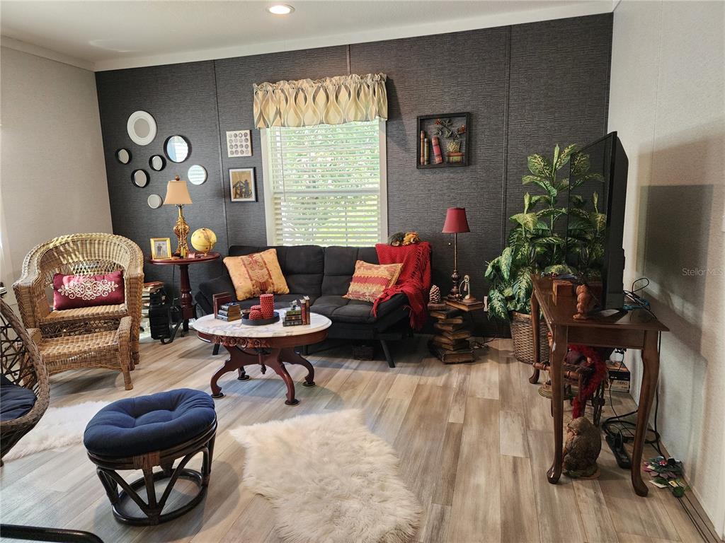A living room features a dark accent wall, a black sofa, wicker chairs, and wood-look flooring — 4150 S SPANIEL TRAIL, INVERNESS, FL