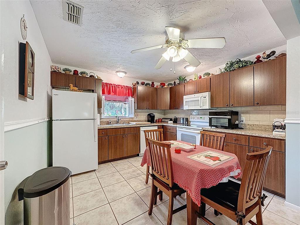 A kitchen with wood cabinets, white appliances, a tiled floor, and a small dining table — 7135 TRENTON PLACE, NEW PORT RICHEY, FL