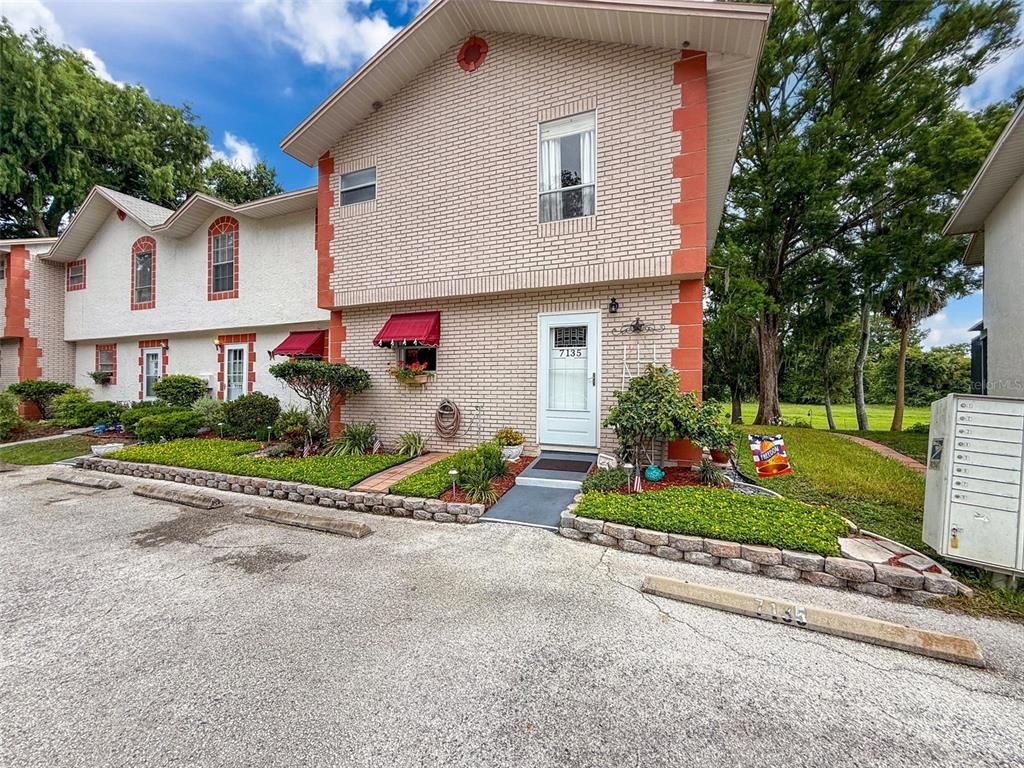 A two-story brick townhouse with a white front door and a small landscaped front yard — 7135 TRENTON PLACE, NEW PORT RICHEY, FL