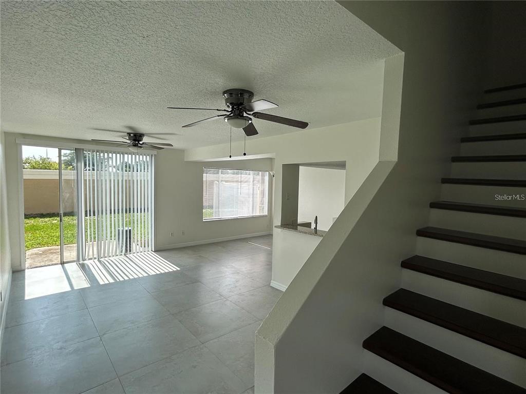 A living area with tile floors, ceiling fans, sliding glass doors, and an adjacent staircase — 202 WASHINGTON PALM LOOP, DAVENPORT, FL