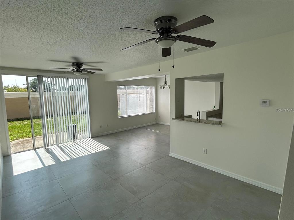 An open-concept living area features gray tile flooring, ceiling fans, and a sliding glass door — 202 WASHINGTON PALM LOOP, DAVENPORT, FL