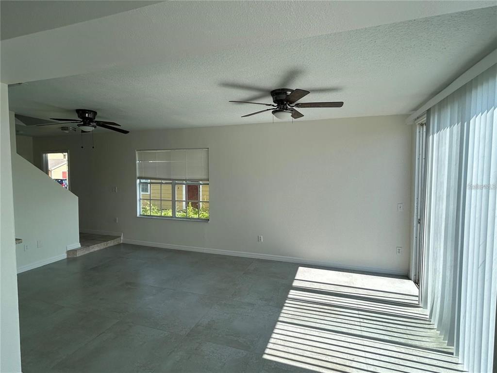 An empty living room features large gray floor tiles, two ceiling fans, and sliding glass doors — 202 WASHINGTON PALM LOOP, DAVENPORT, FL