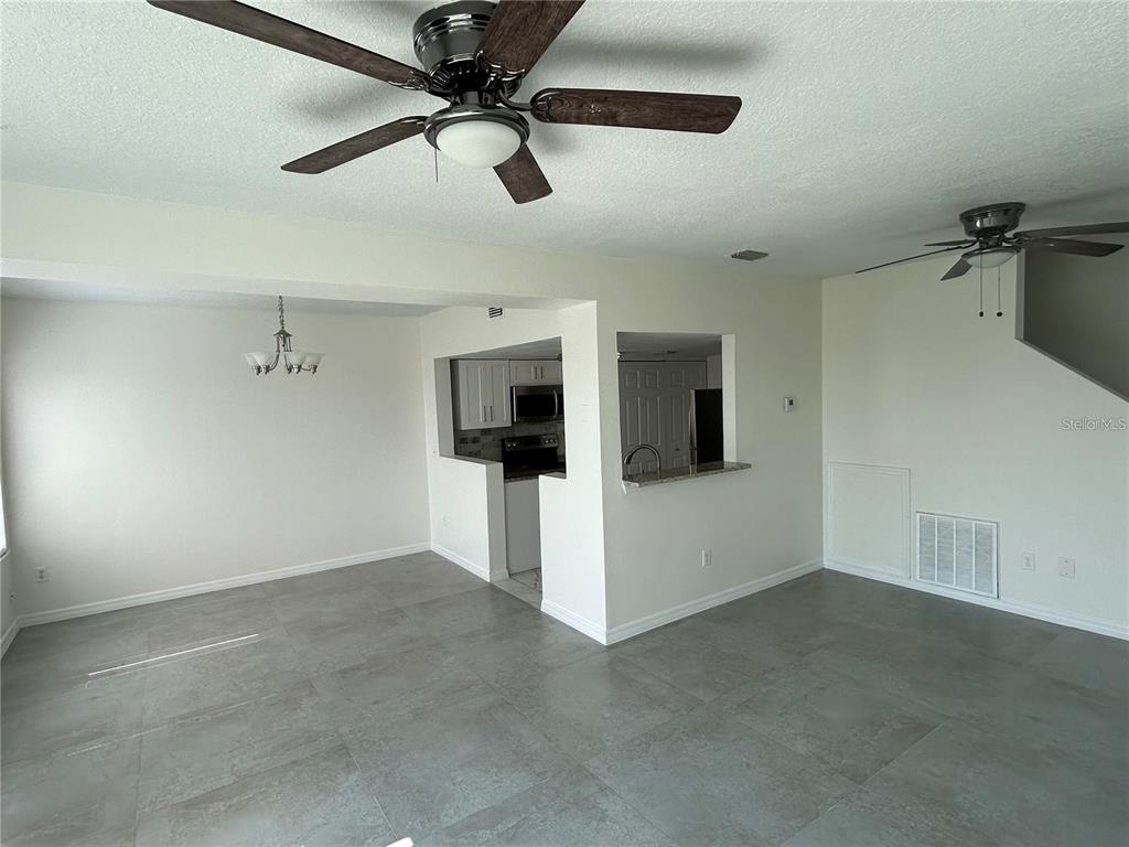 An open-concept living and dining area features gray tile flooring and two ceiling fans — 202 WASHINGTON PALM LOOP, DAVENPORT, FL