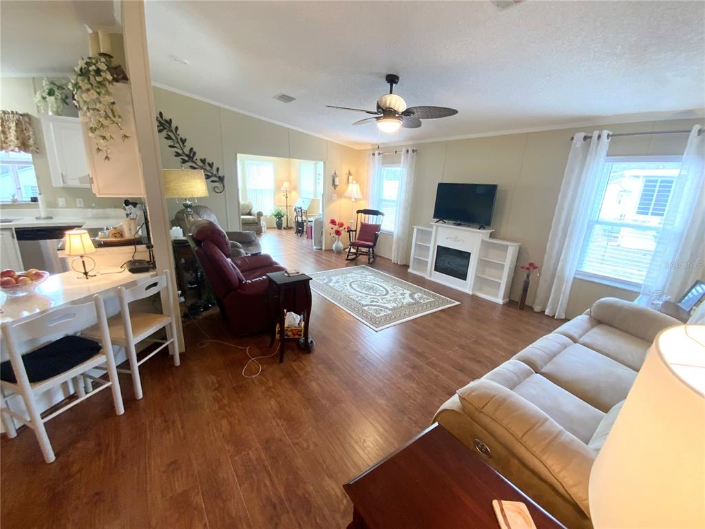 A living room with wood-look flooring, a fireplace, and an open layout connecting to the kitchen — 4842 SE 130TH PLACE, BELLEVIEW, FL