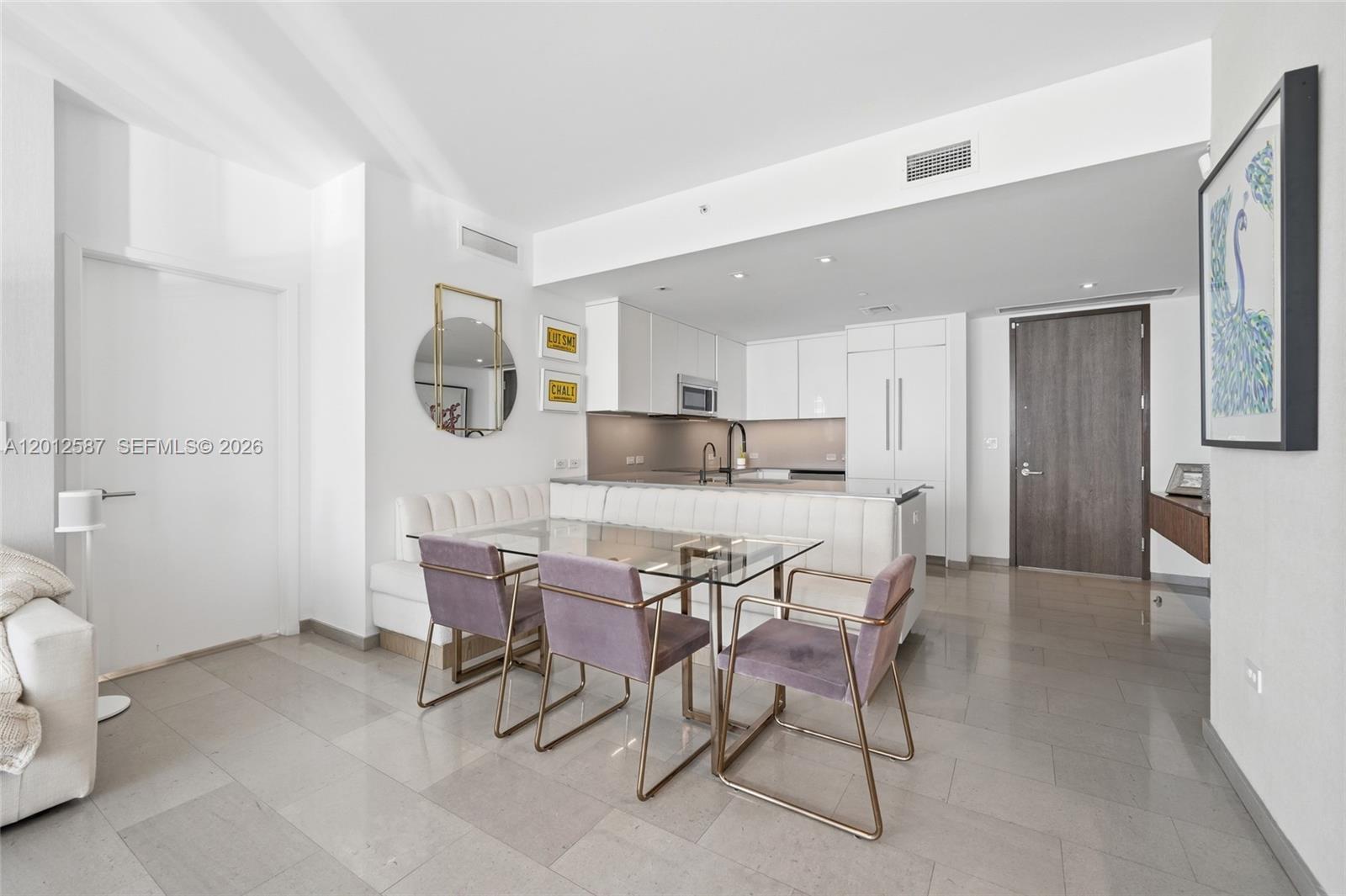 A modern kitchen and dining area feature a glass table, upholstered chairs, and white cabinetry — 68 SE 6th St # 1904, Miami FL 33131, MIAMI, FL