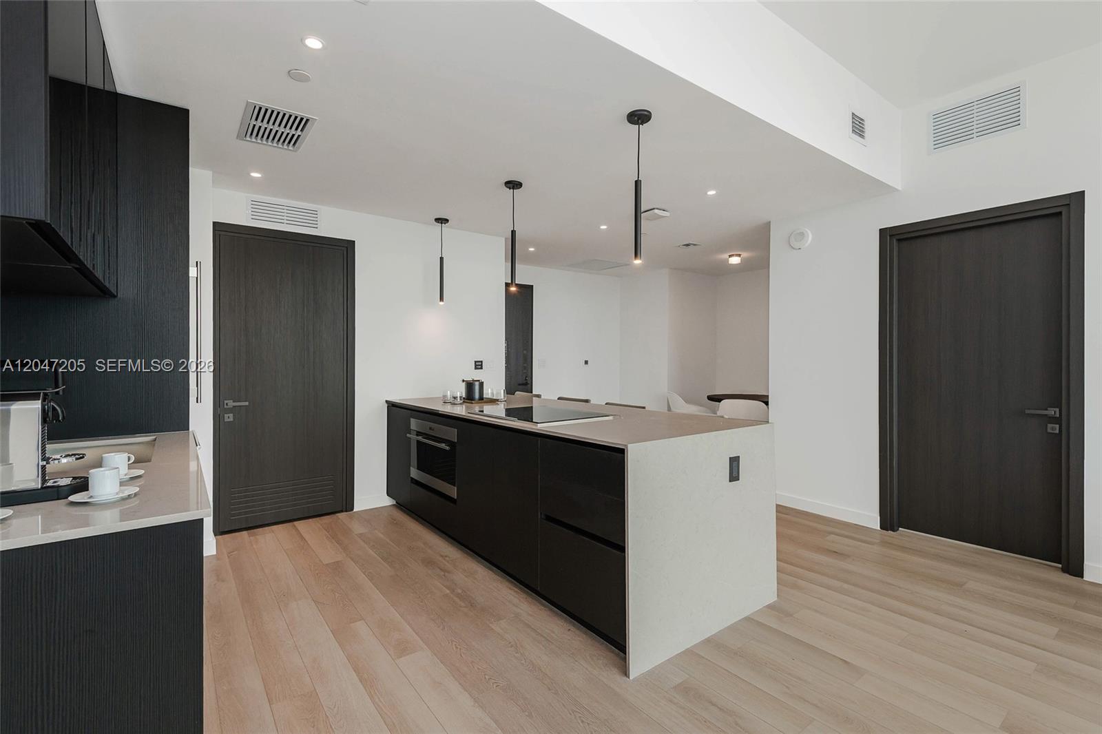 A modern kitchen features a dark island with a cooktop, light countertops, and wood flooring — 20 NE 11 ST # 4901, Miami FL 33132, MIAMI, FL