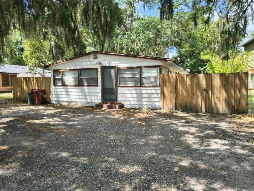 A single-story house with white siding and a wooden fence sits on a gravel lot — 611 SHORT STREET, PLANT CITY, FL