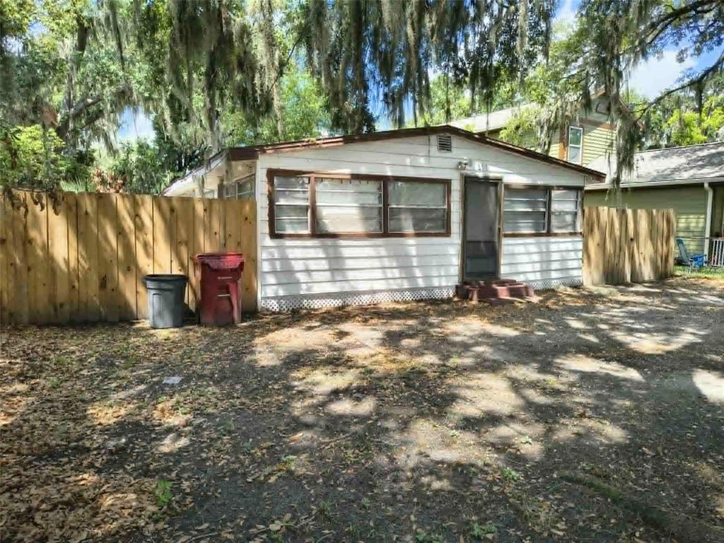 A single-story white house with brown trim sits behind a wooden fence and gravel yard — 611 SHORT STREET, PLANT CITY, FL