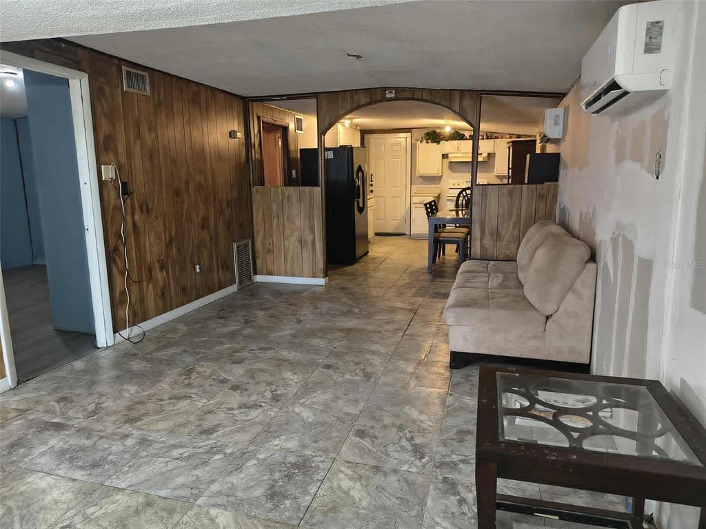 A living room with wood-paneled walls, tile flooring, a beige sofa, and an arched entryway — 611 SHORT STREET, PLANT CITY, FL