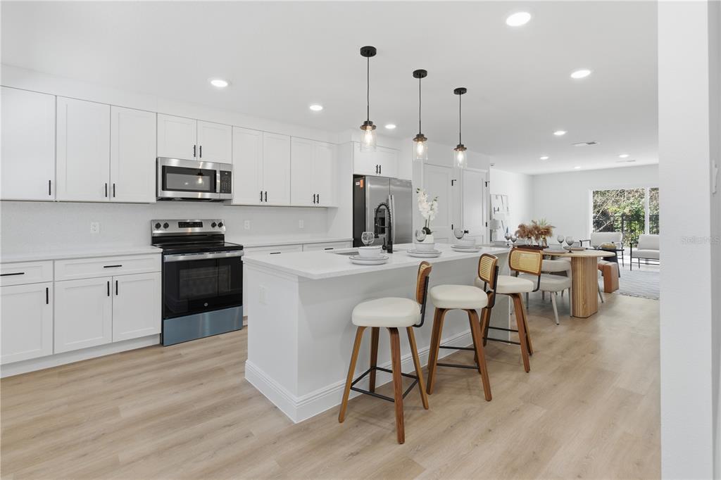 A modern kitchen features white cabinetry, a central island with bar stools, and light flooring — 719 CLEMSON DRIVE, ALTAMONTE SPRINGS, FL