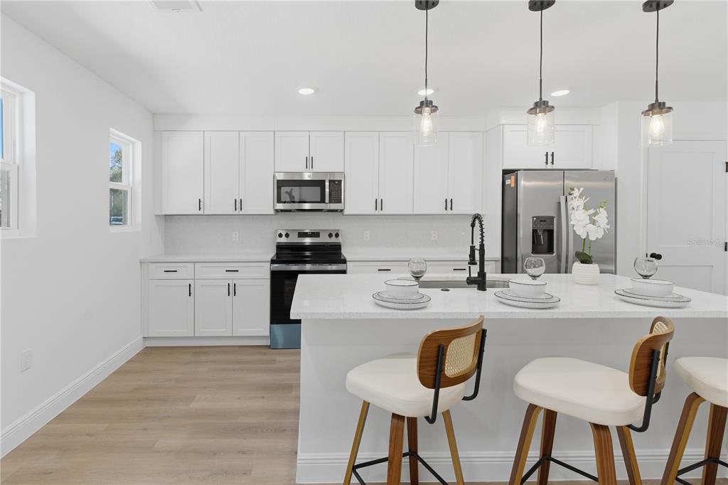 A modern kitchen features white cabinets, stainless steel appliances, a quartz island, and pendant lighting — 719 CLEMSON DRIVE, ALTAMONTE SPRINGS, FL