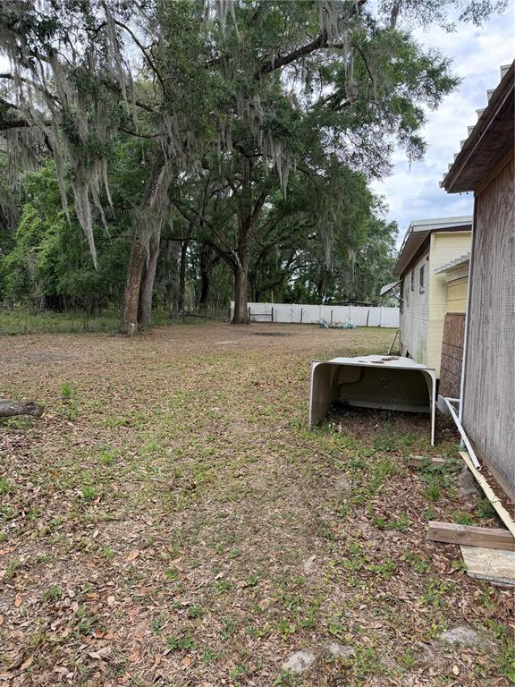 A grassy backyard features large trees with Spanish moss and a white privacy fence — 11259 NE 10TH TERRACE, OXFORD, FL