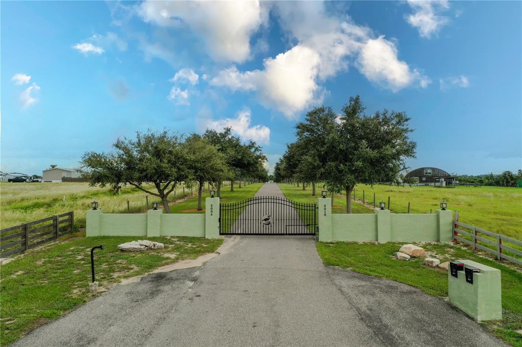 A paved driveway leads to a gated entrance with a green stucco wall and trees — 8010 LAKE LOWERY ROAD, HAINES CITY, FL