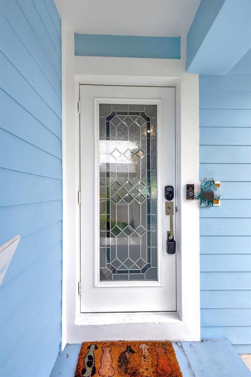 A white front door with a decorative glass insert is set against light blue siding — 1131 Surf Road, Singer Island FL 33404, SINGER ISLAND, FL