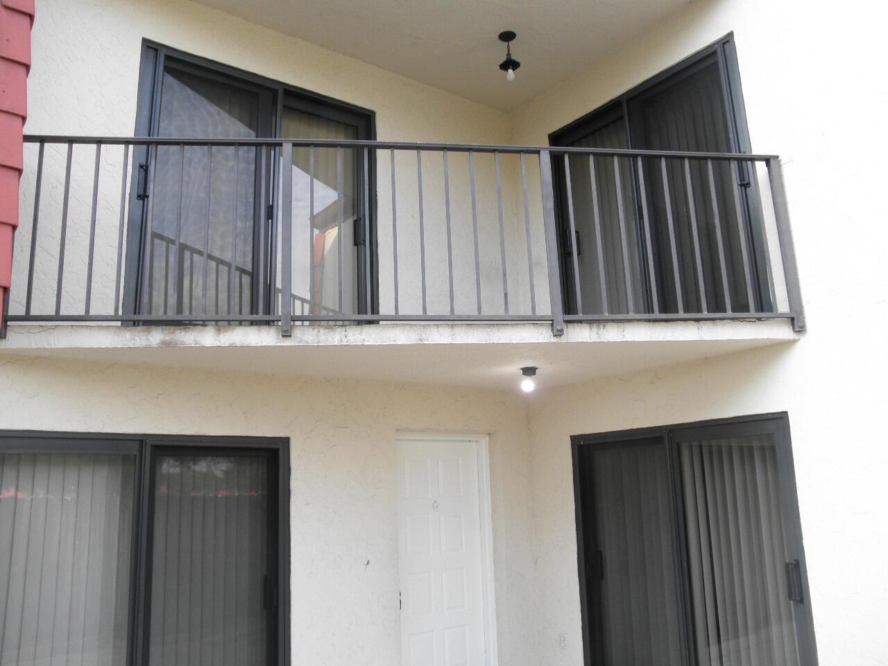 A two-story building exterior featuring a balcony with metal railings and sliding glass doors — WEST PALM BEACH, FL
