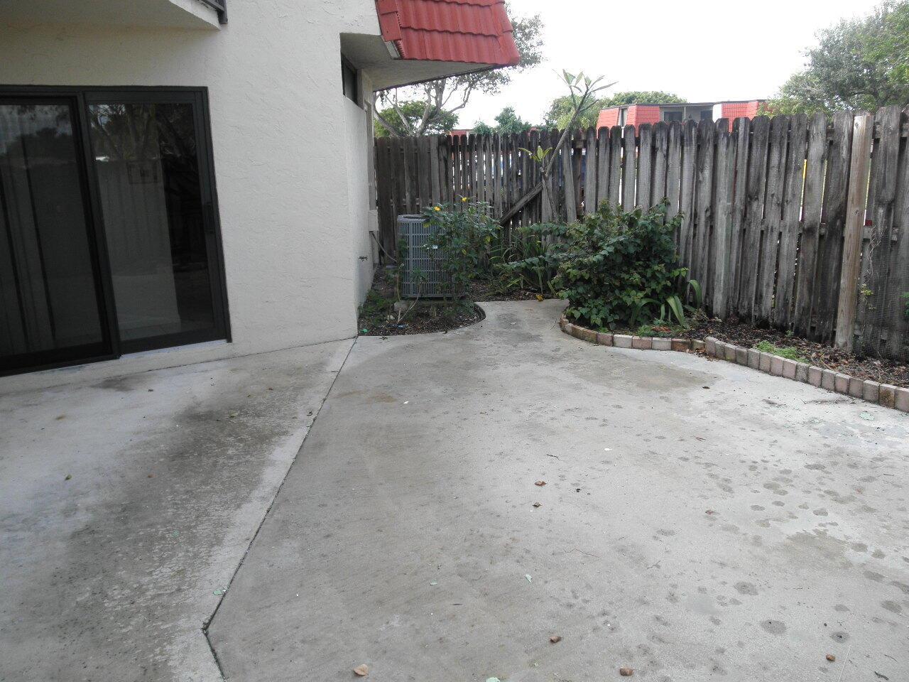 A concrete patio sits beside a building exterior with a sliding glass door and fence — WEST PALM BEACH, FL