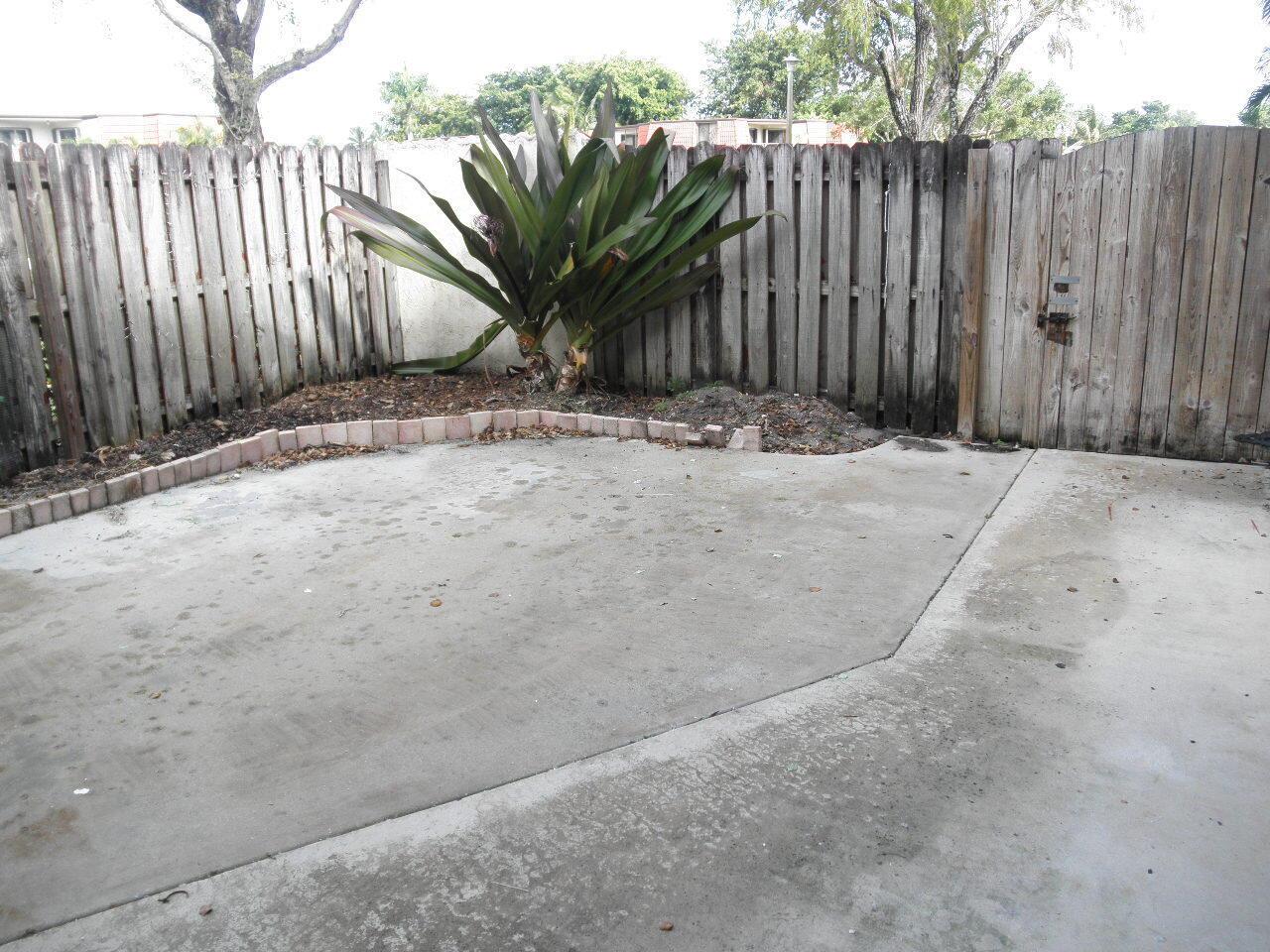 A concrete patio features a small garden bed with a large plant and wooden fencing — WEST PALM BEACH, FL