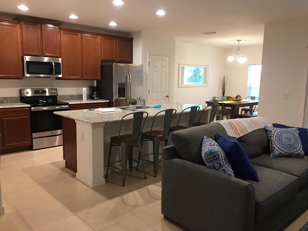 An open-concept kitchen with granite countertops and stainless steel appliances overlooks a living room area — 258 ANNABELLE WAY, DAVENPORT, FL
