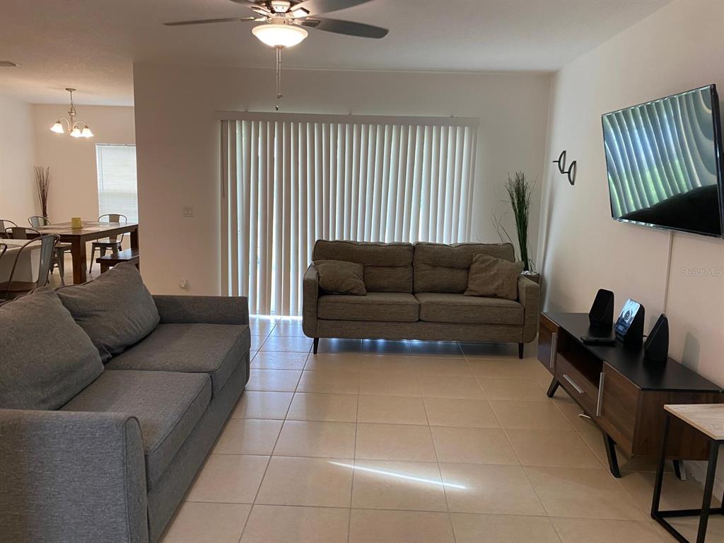 A living room features a gray sofa, a tan loveseat, tile flooring, and a wall-mounted television — 258 ANNABELLE WAY, DAVENPORT, FL