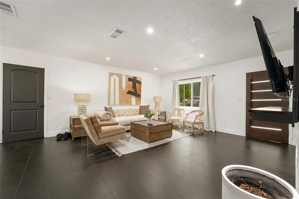 A living room features dark tile flooring, white walls, a tufted sofa, and a television — 1214 NW 55TH TERRACE, GAINESVILLE, FL