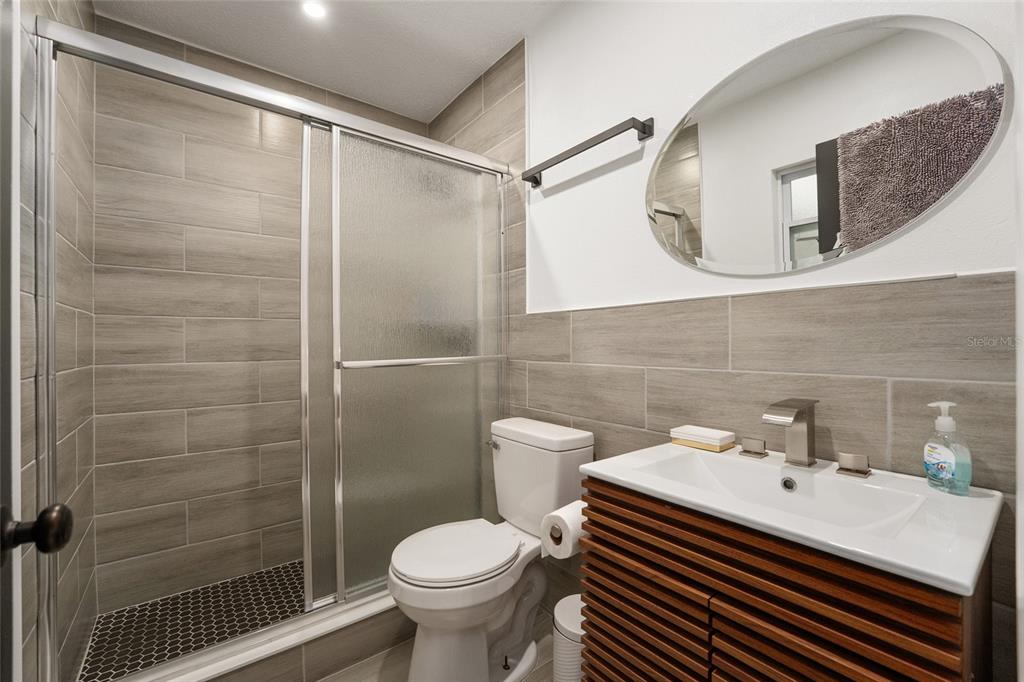 A bathroom features a walk-in shower with glass doors, a toilet, and a wood-slatted vanity — 1214 NW 55TH TERRACE, GAINESVILLE, FL