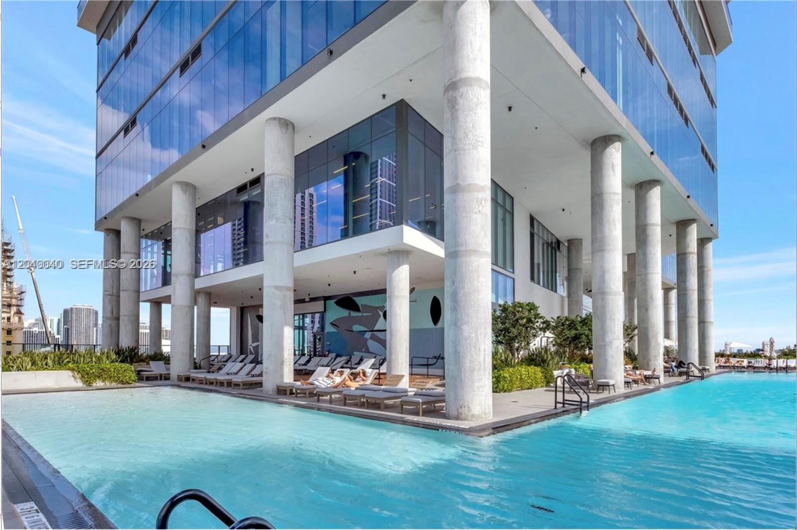 A modern high-rise building features a large outdoor swimming pool with lounge chairs and columns — 398 NE 5th St, Miami FL 33132, MIAMI, FL