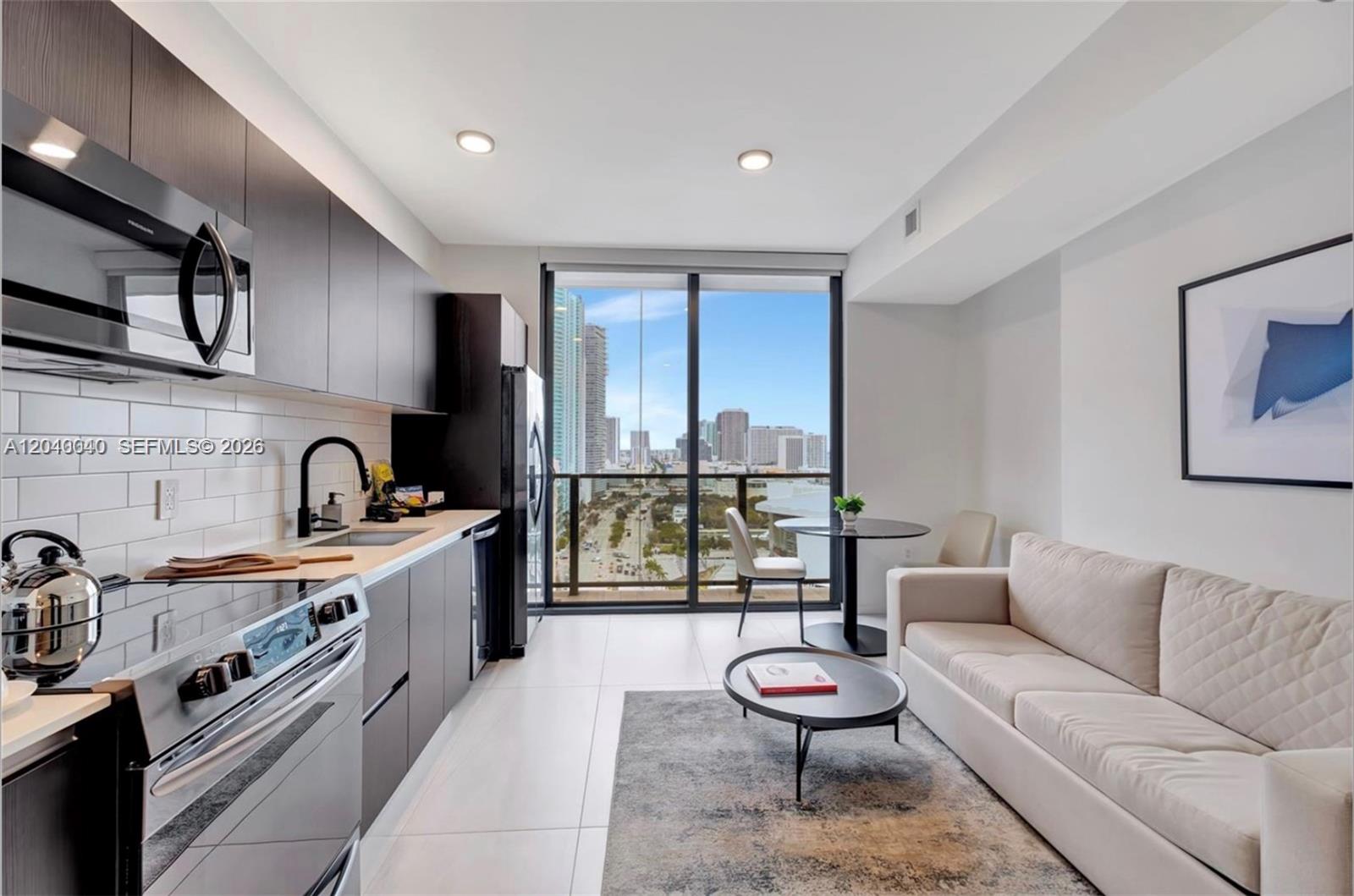 A modern studio apartment features a kitchen with dark cabinets, a sofa, and a balcony — 398 NE 5th St, Miami FL 33132, MIAMI, FL
