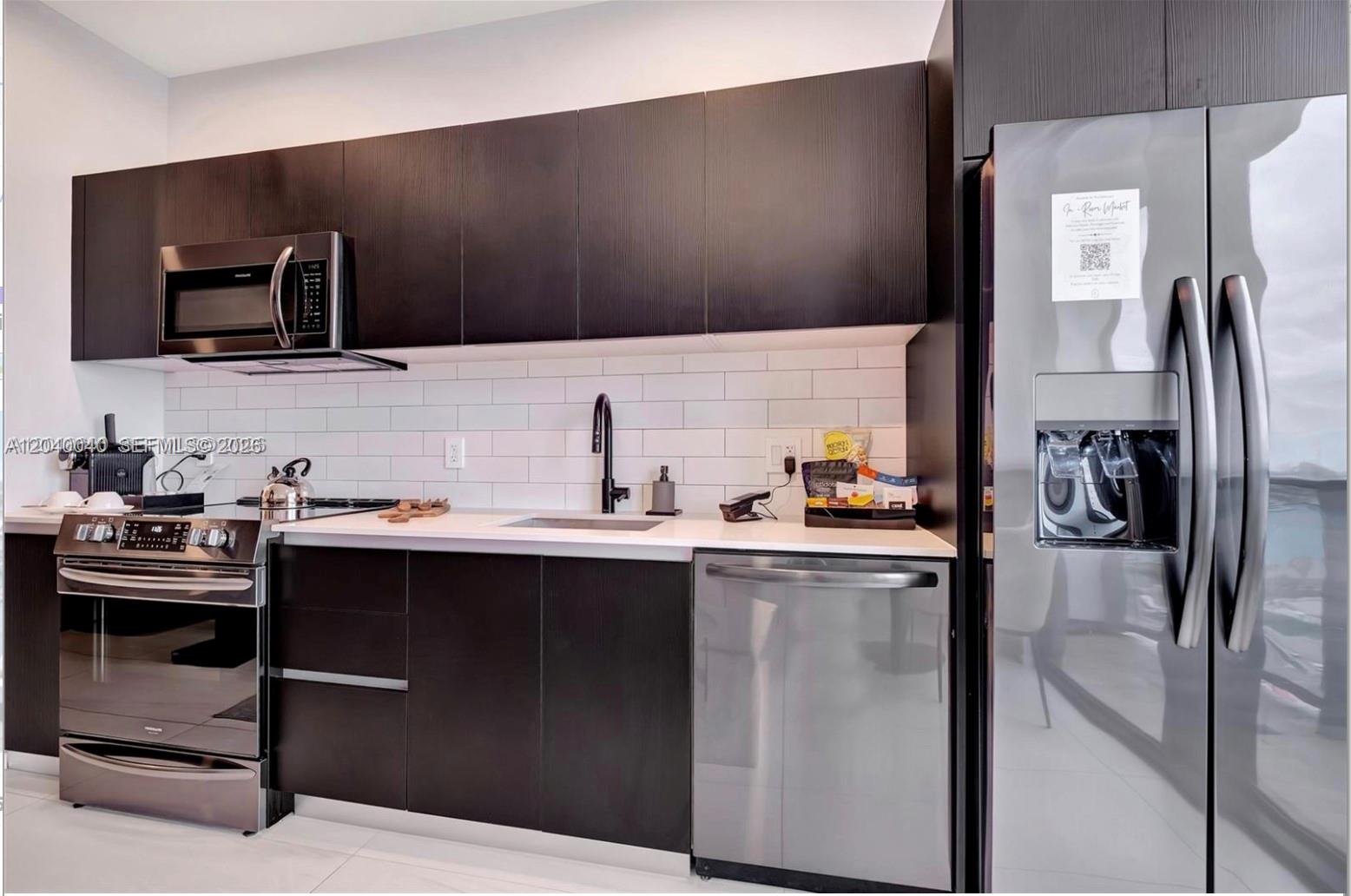 A modern kitchen features dark wood cabinets, stainless steel appliances, and white subway tile backsplash — 398 NE 5th St, Miami FL 33132, MIAMI, FL