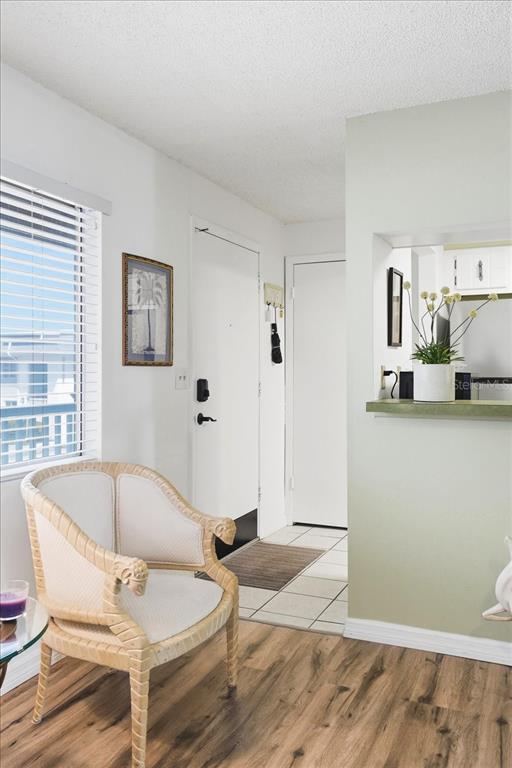 A room features a wicker chair, wood-look flooring, a white door, and a kitchen pass-through — 22375 EDGEWATER DRIVE UNIT 256, PUNTA GORDA, FL