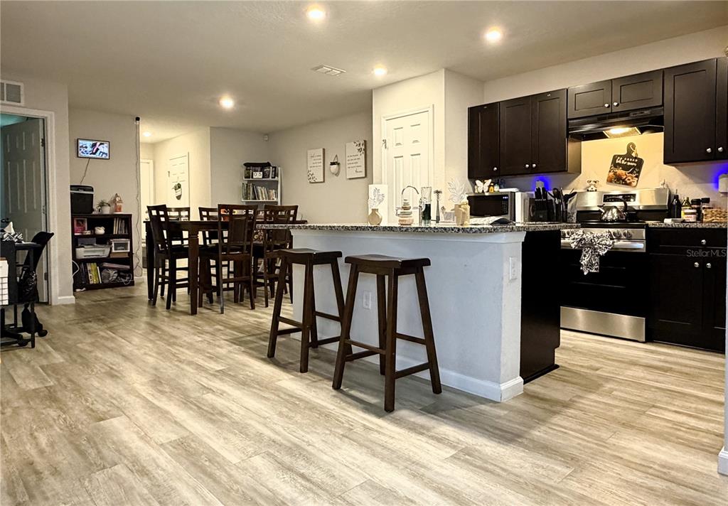 An open-concept kitchen and dining area featuring dark cabinetry, a breakfast bar, and wood-look flooring — 8139 VINING STREET, JACKSONVILLE, FL