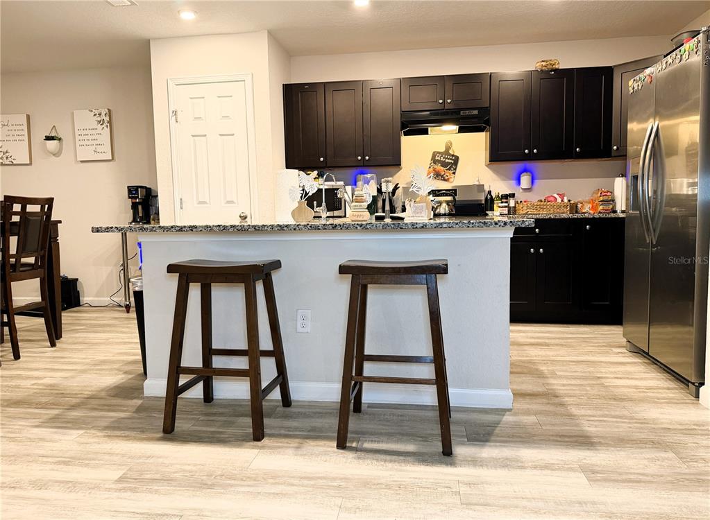 A kitchen features dark cabinets, granite countertops, a breakfast bar with two stools, and wood-look flooring — 8139 VINING STREET, JACKSONVILLE, FL