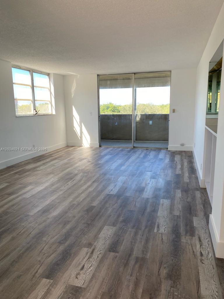 An empty living room features wood-look flooring, a sliding glass door, and a side window — 406 NW 68th Ave # 526, Plantation FL 33317, PLANTATION, FL