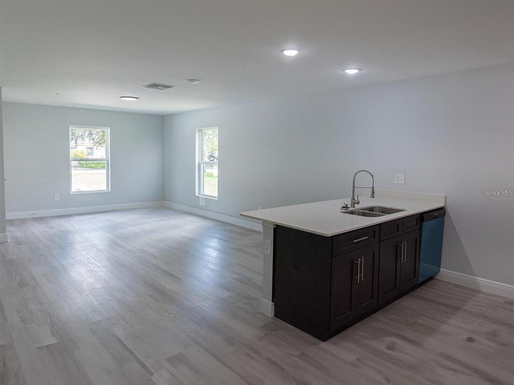 An open-concept room features light wood-look flooring, white walls, and a dark kitchen island — 1725 CRYSTAL GROVE DRIVE UNIT 1727, LAKELAND, FL
