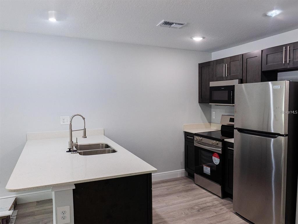 A kitchen features dark cabinets, stainless steel appliances, and a white quartz-topped island with sink — 1725 CRYSTAL GROVE DRIVE UNIT 1727, LAKELAND, FL