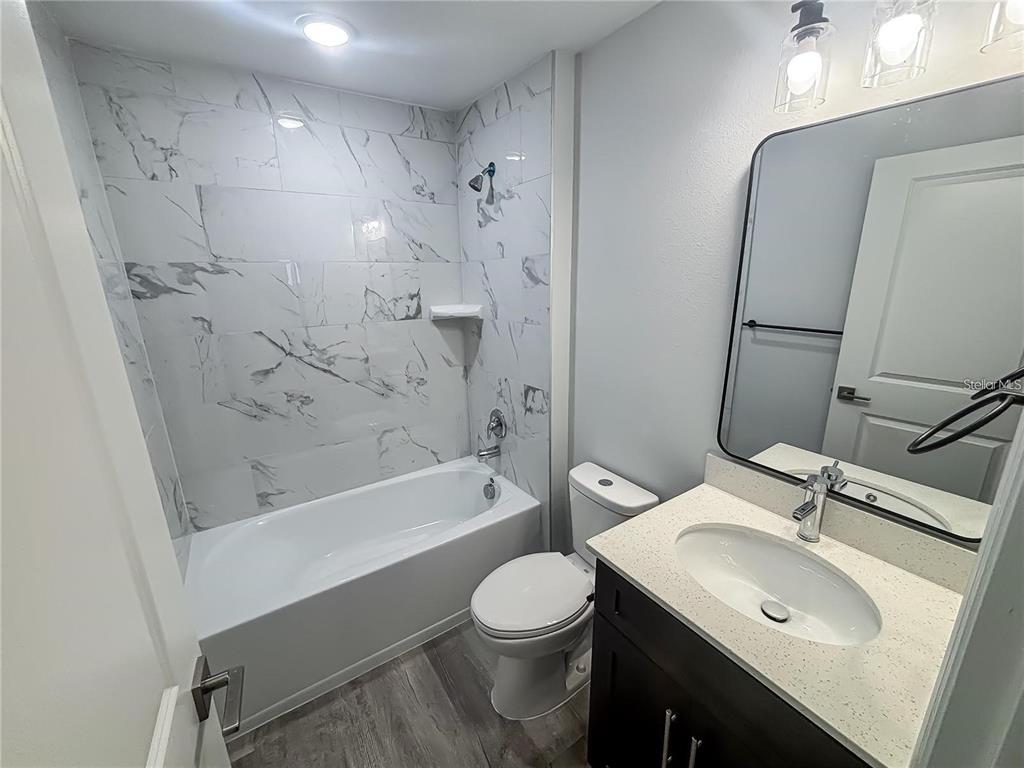 A bathroom features a marble-tiled shower-tub combo, a white toilet, and a vanity with mirror — 1725 CRYSTAL GROVE DRIVE UNIT 1727, LAKELAND, FL