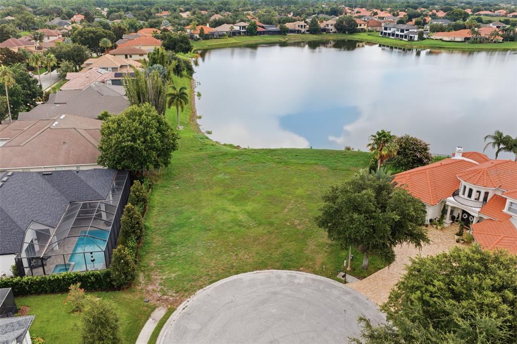An aerial view shows a vacant grassy lot situated between two houses and a lake — 10341 ALTRARA WAY, TRINITY, FL