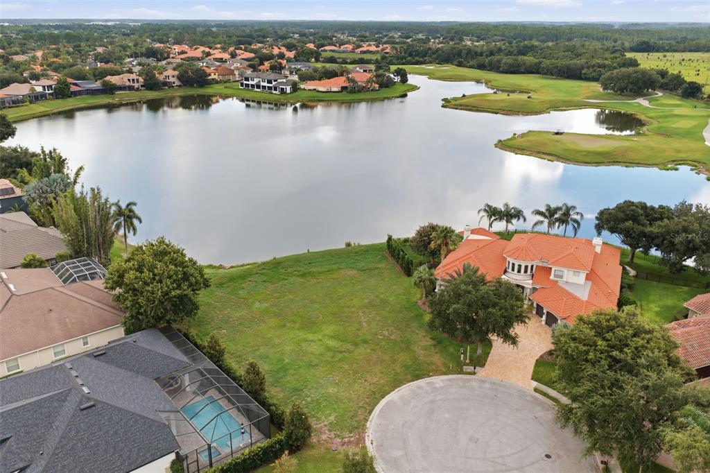 An aerial view shows a vacant grassy lot situated between two houses near a lake — 10341 ALTRARA WAY, TRINITY, FL