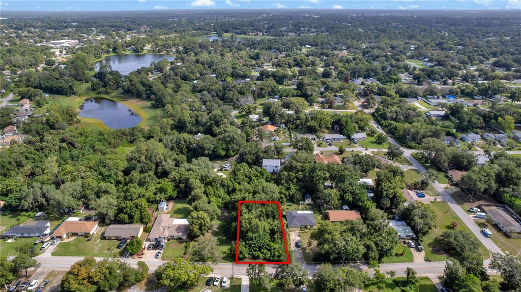 An aerial view shows a rectangular, tree-covered vacant lot outlined in red within a neighborhood — 132 COLOMBA ROAD, DEBARY, FL