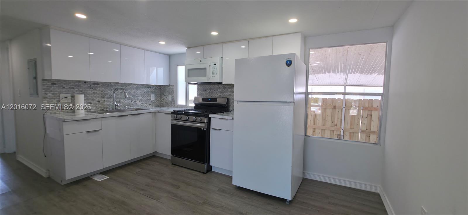 A kitchen features white cabinets, stainless steel appliances, a tiled backsplash, and wood-look flooring — 1730 SW 85th Ave, Davie FL 33324, DAVIE, FL