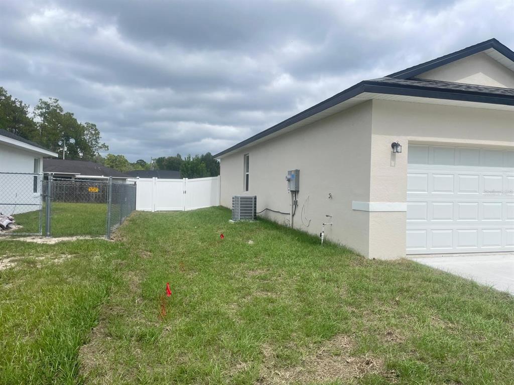 The exterior side of a house features a white garage door, HVAC unit, and fencing — 723 MARION OAK TRAIL, OCALA, FL