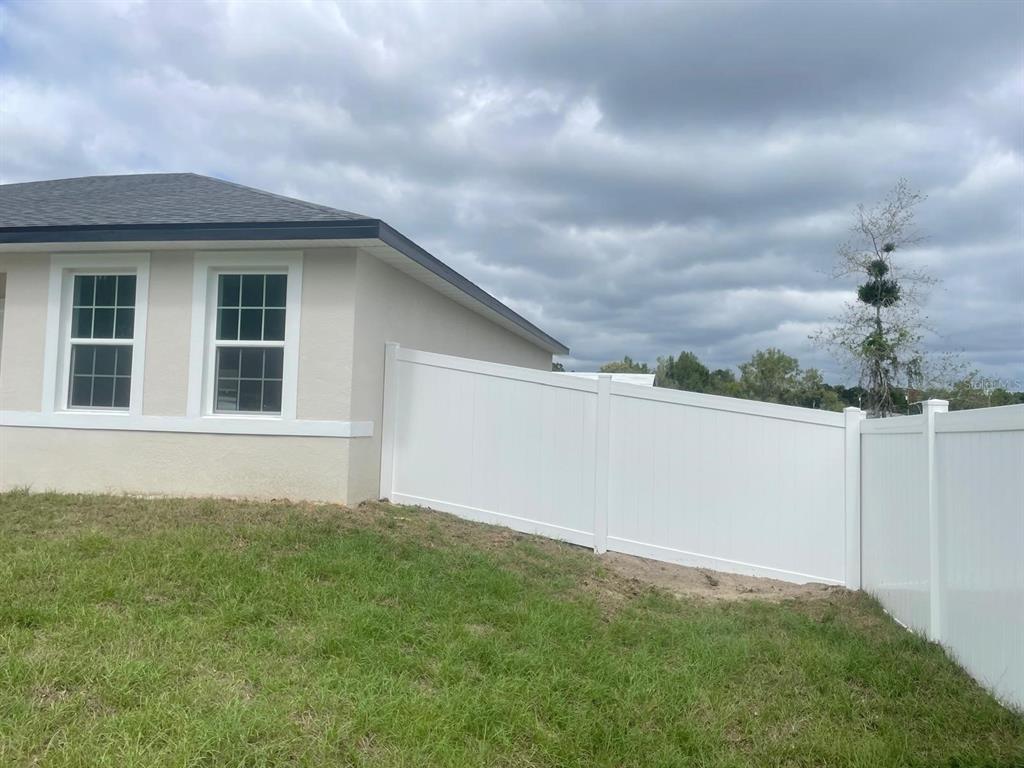 A white vinyl privacy fence runs along the side of a beige house exterior — 723 MARION OAK TRAIL, OCALA, FL