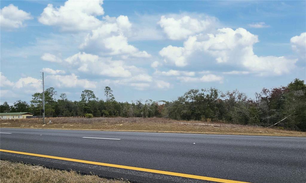 A vacant, grassy lot sits alongside a paved road under a blue, cloudy sky — 0000 NE HIGHWAY 27 ALT, WILLISTON, FL