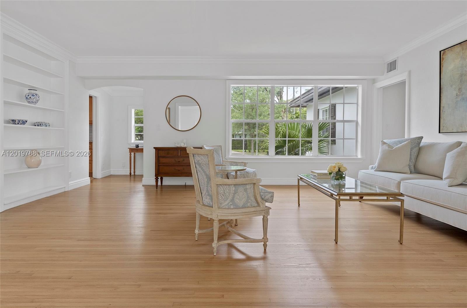 A bright living room features hardwood floors, a large window, built-in shelves, and neutral furniture — 1540 Urbino Ave, Coral Gables FL 33146, CORAL GABLES, FL
