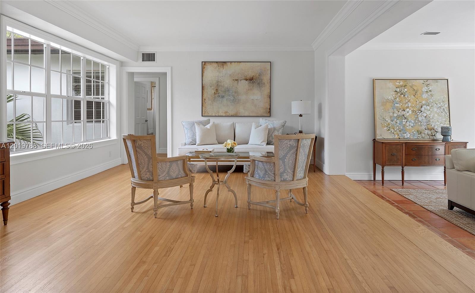 A living room features light wood floors, two patterned armchairs, a sofa, and artwork — 1540 Urbino Ave, Coral Gables FL 33146, CORAL GABLES, FL